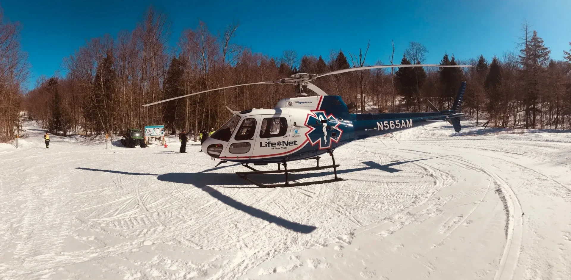 A helicopter is parked on the snow near trees.