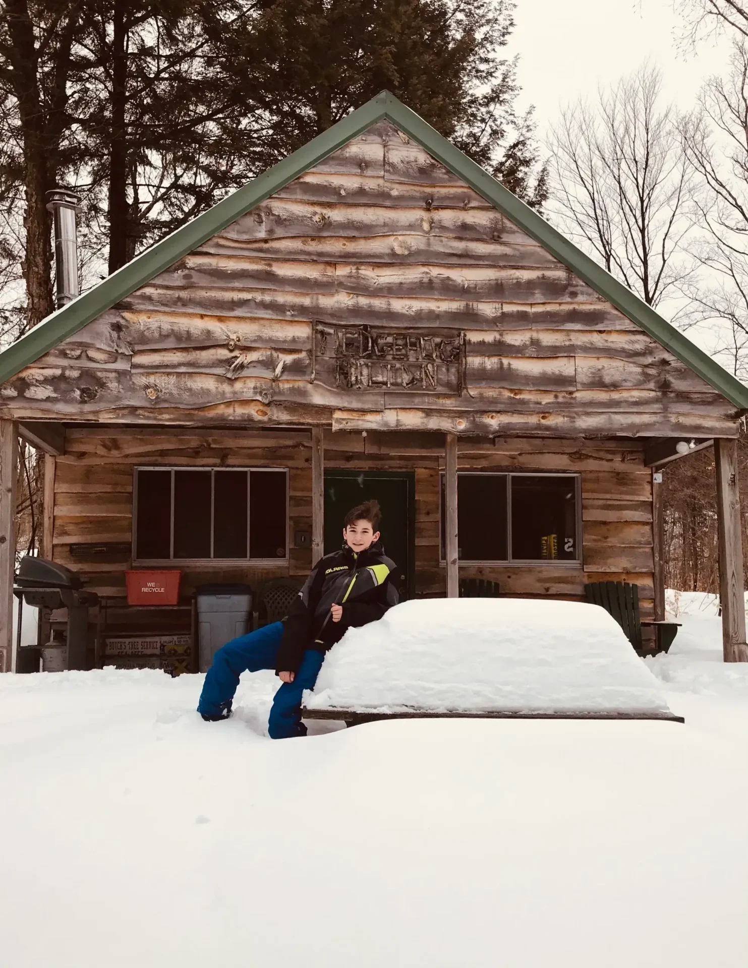 A man sitting in the snow outside of a log cabin.